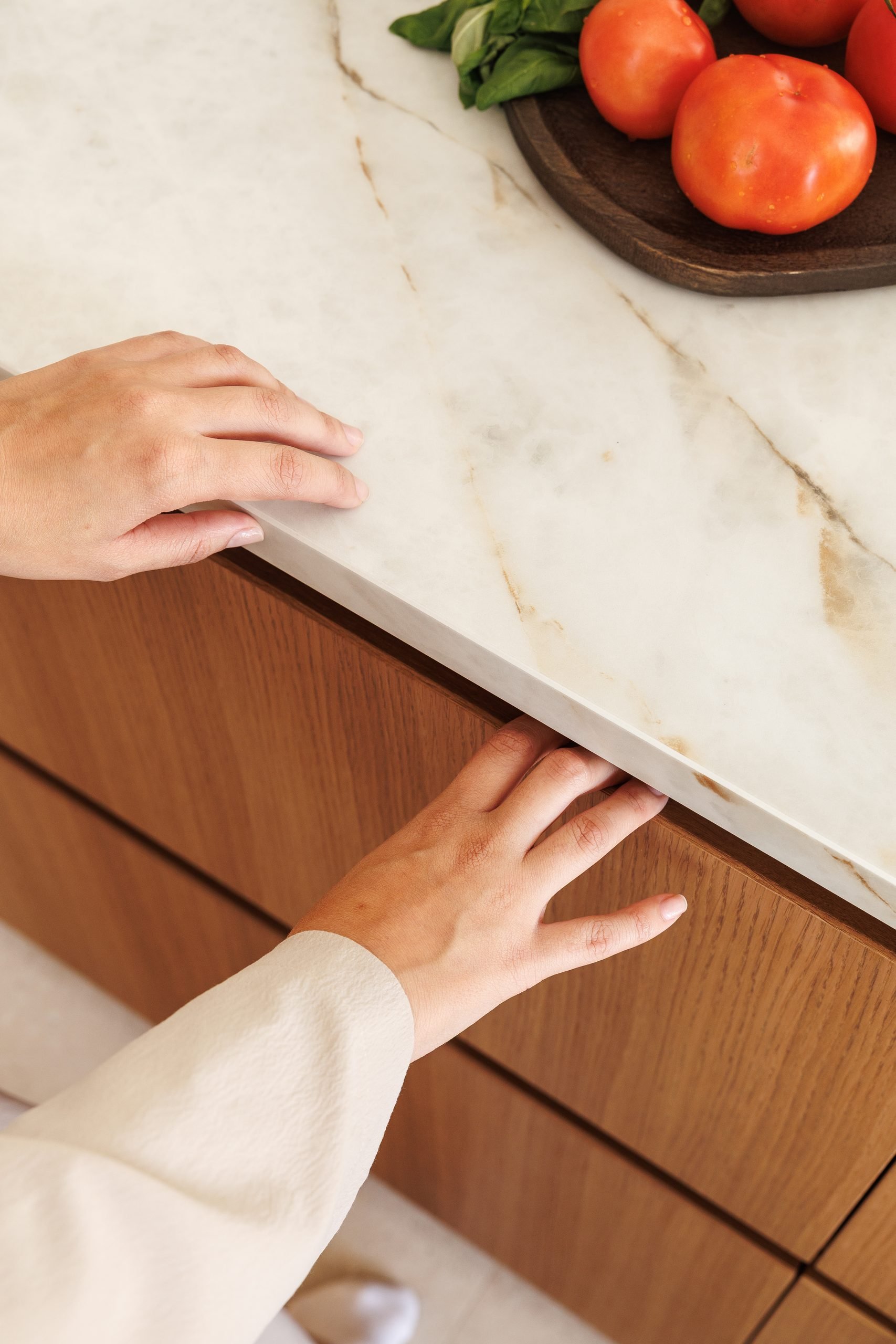 Manos sobre encimera de piedra veteada y frente de madera — B2 Invest Cocina, Costa del Sol. Fotografía de Pedro Jaén
