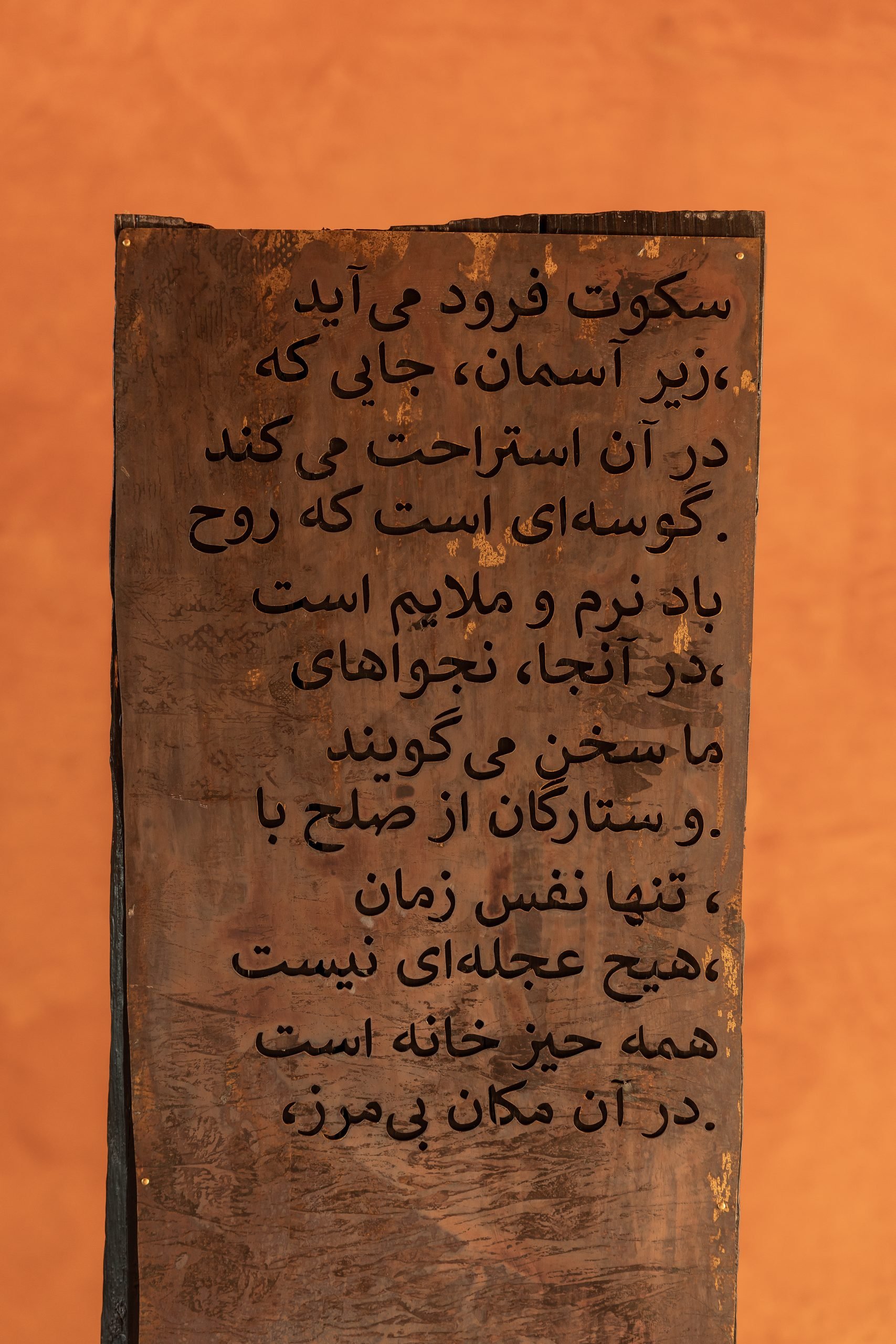 Tabla de madera con poema en caligrafía persa sobre muro ocre — Endless Istán, Istán, Málaga. Fotografía de Pedro Jaén