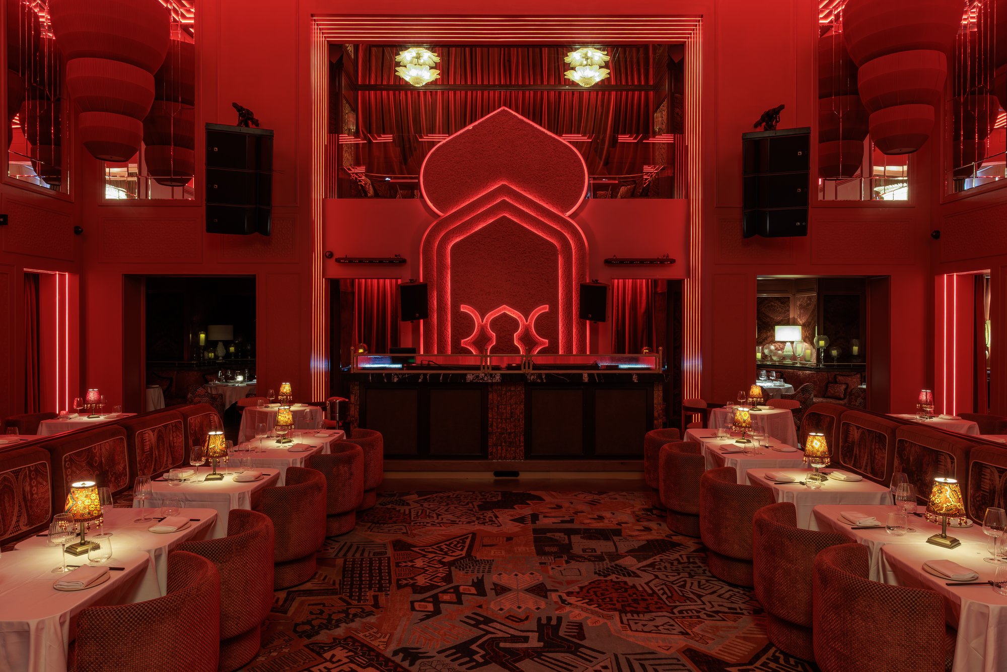 Comedor simétrico ante el escenario con arco de neón y alfombra estampada — Motel · Nuevo, Marbella. Fotografía de Pedro Jaén